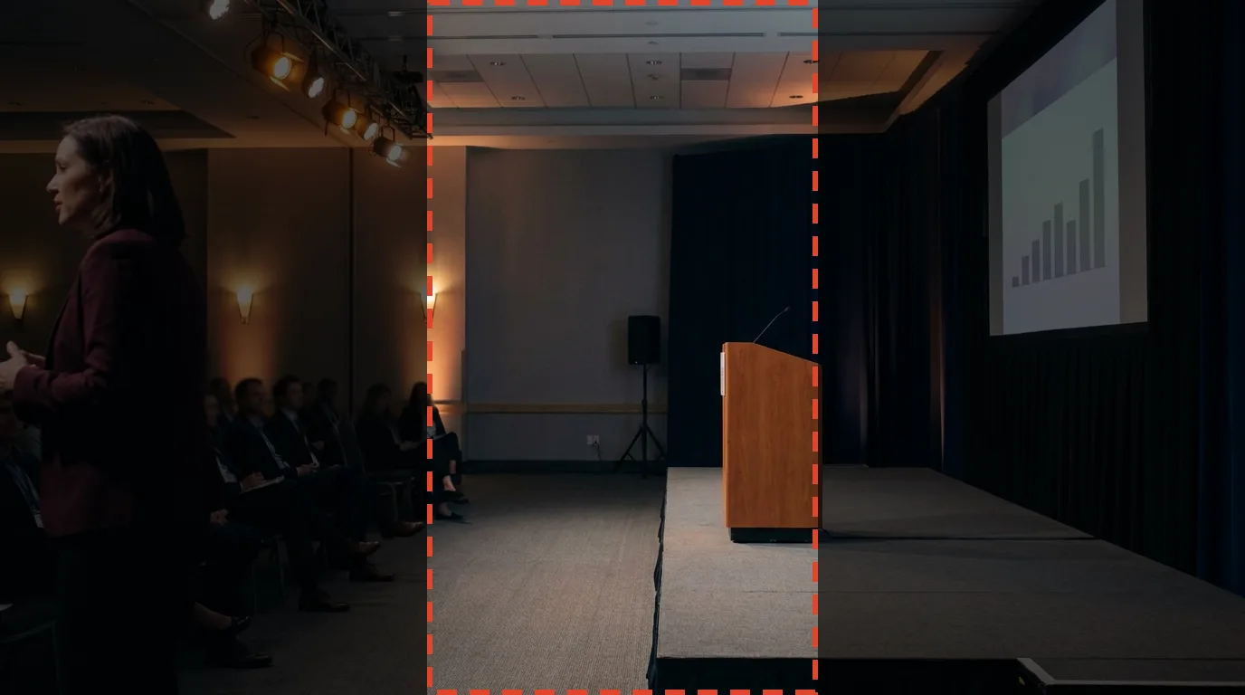 A widescreen frame with the speaker at the far left edge and the vertical crop region falling on an empty lectern